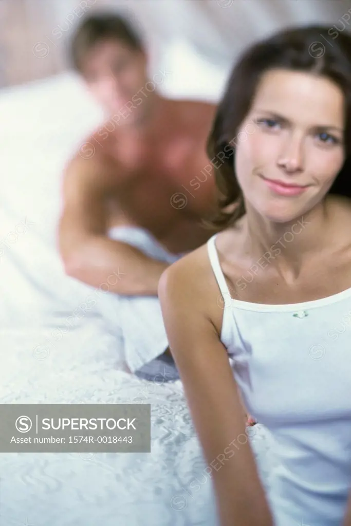 Portrait of a young woman smiling with a young man sitting behind her in bed