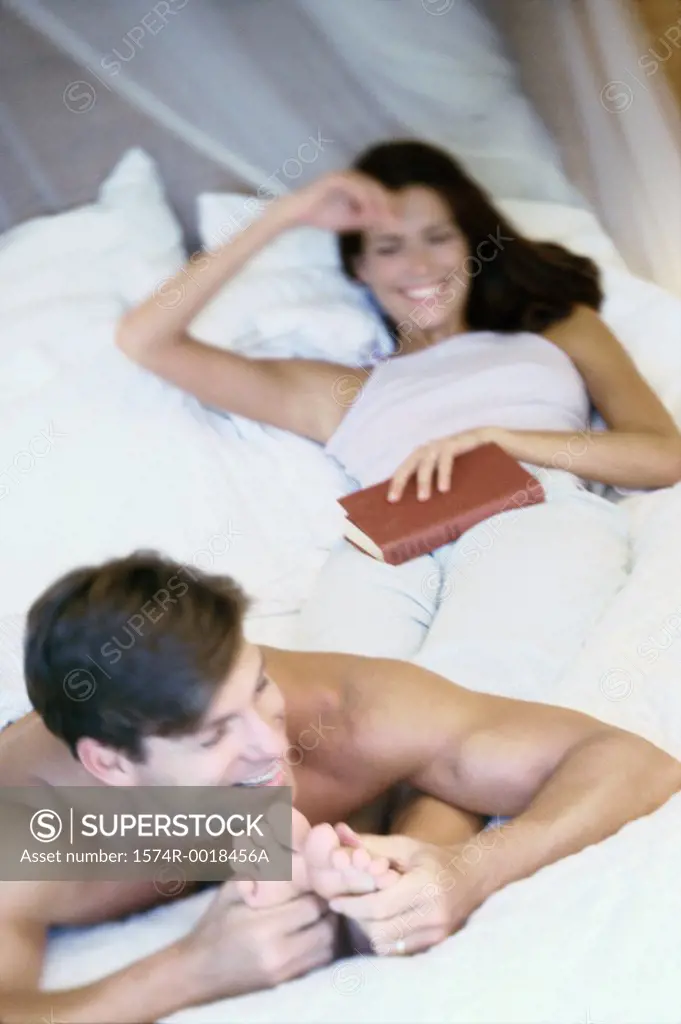Young man massaging the feet of a young woman in bed
