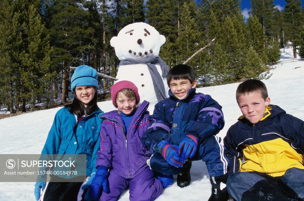 Two boys and two girls kneeling in front of a snowman