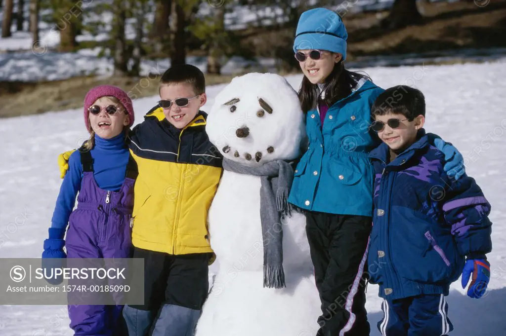 Two boys and two girls standing beside a snowman