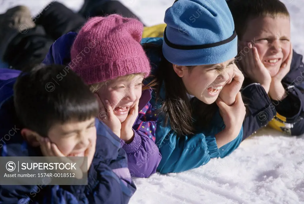 Close-up of two boys and two girls lying in snow with their hands on their chins