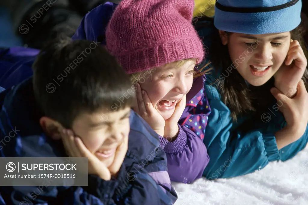 Close-up of two girls and a boy lying in the snow