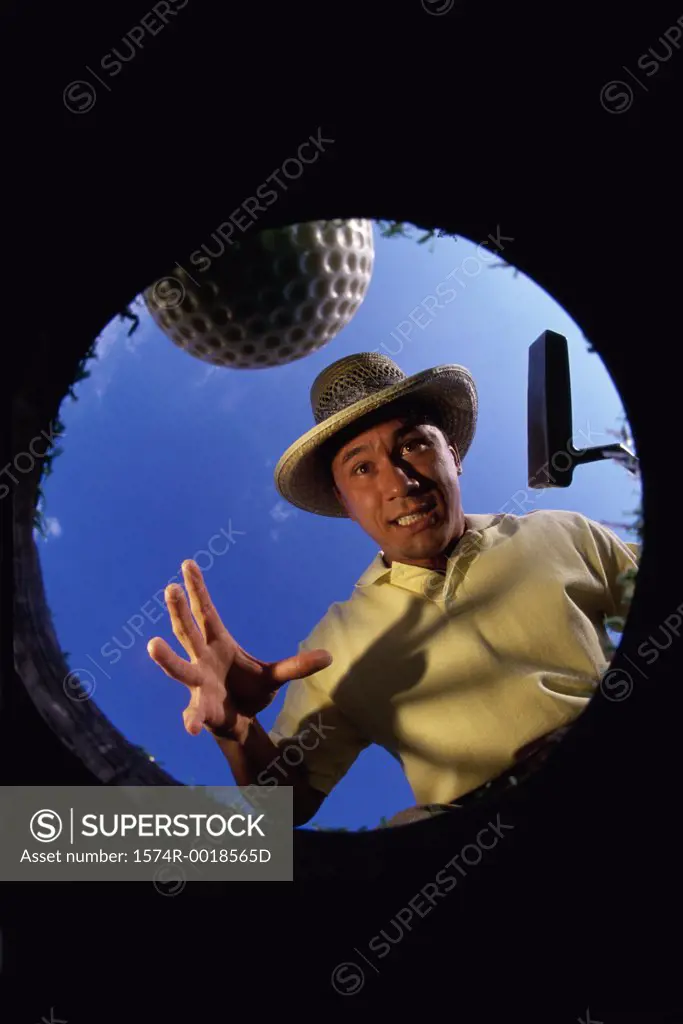 Low angle view of a young man playfully coaxing a golf ball into a hole