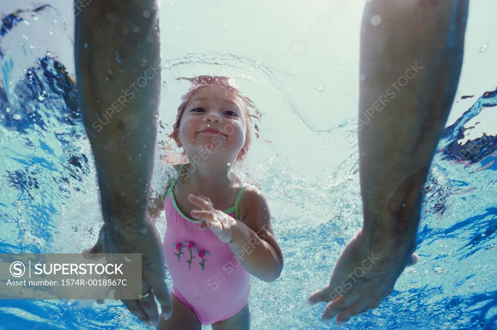 Close-up of father's hands reaching out to his daughter underwater