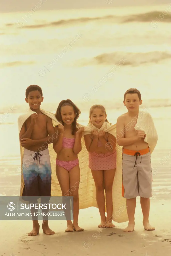 Portrait of two boys and two girls standing with a blanket on the beach