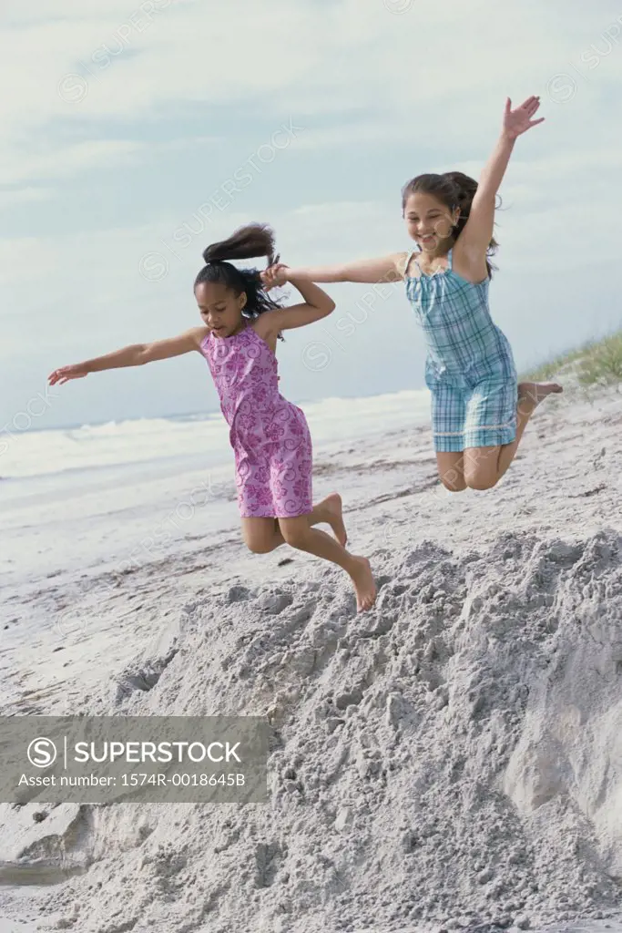 Low angle view of two girls jumping on the beach