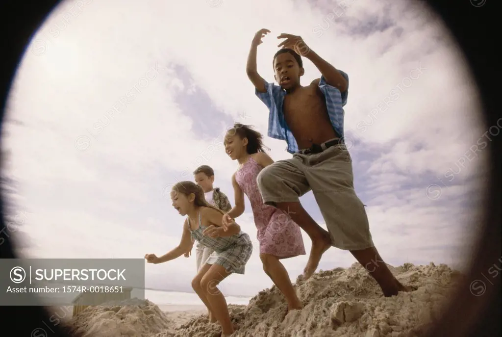 Low angle view of two boys and two girls jumping on the beach