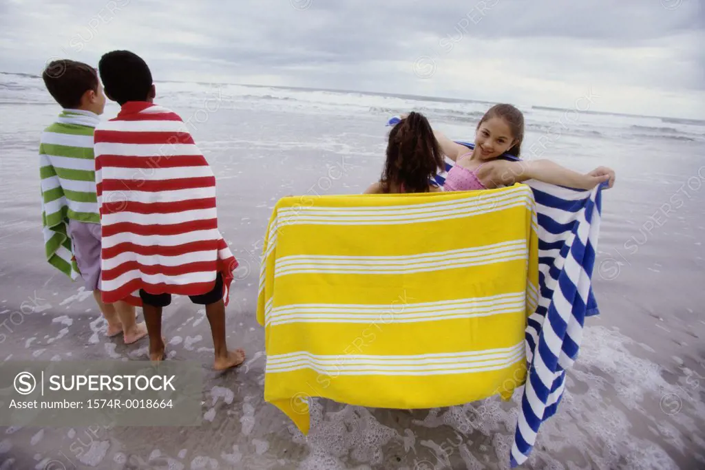 Two boys and two girls standing with towels on the beach