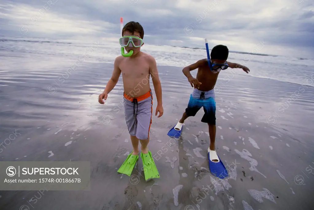 Two boys wearing snorkels and flippers walking on the beach