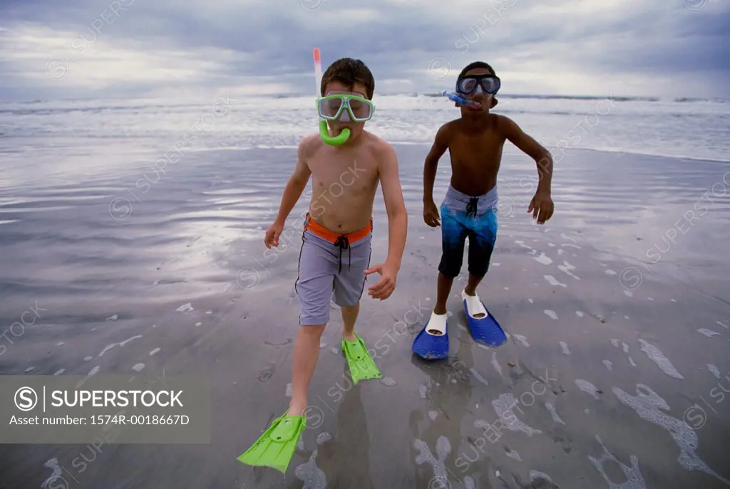 Two boys wearing snorkels and flippers walking on the beach