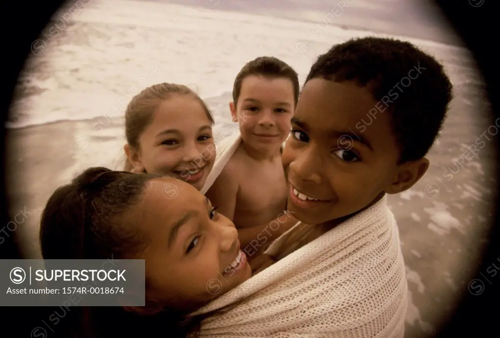 Close-up of two boys and two girls wrapped in a blanket on the beach
