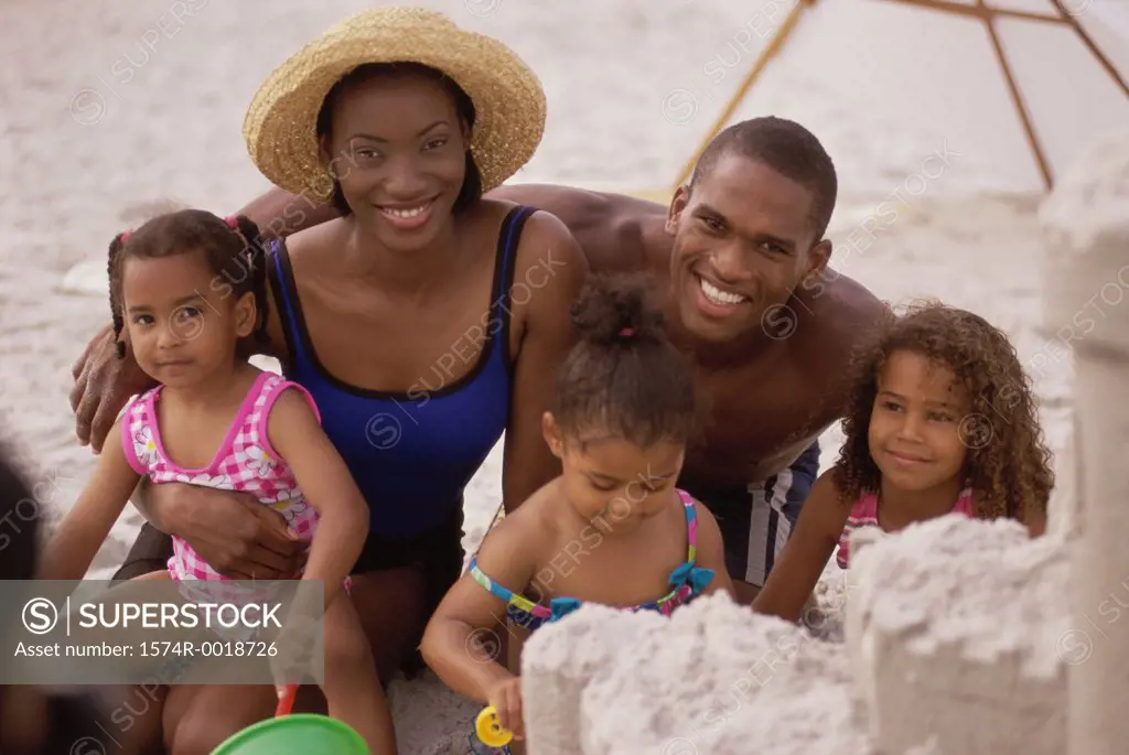 Parents and their three daughters making a sand castle on the beach