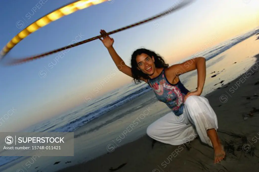 Portrait of a young woman spinning a hula hoop at the beach