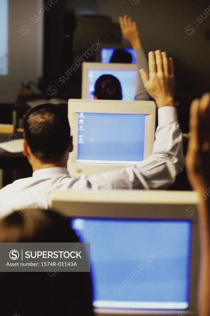 Business executives sitting in front of computer monitors raising their hands at a training class