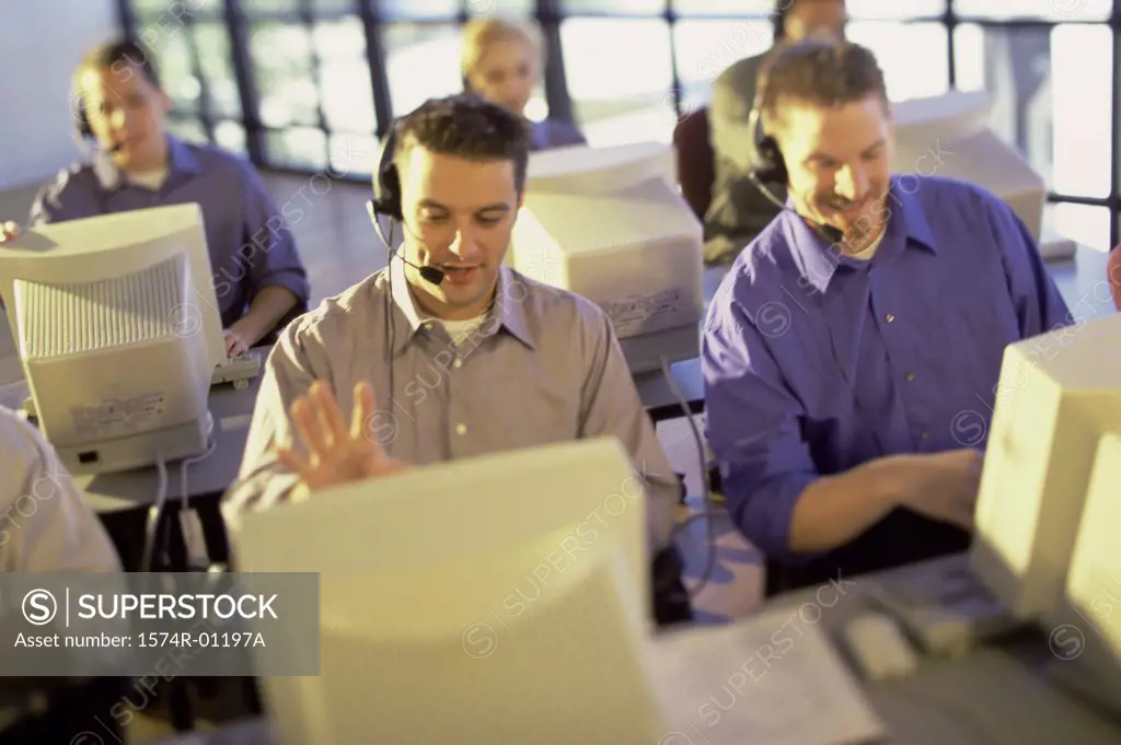 Group of customer service representatives sitting in front of computer monitors wearing headsets