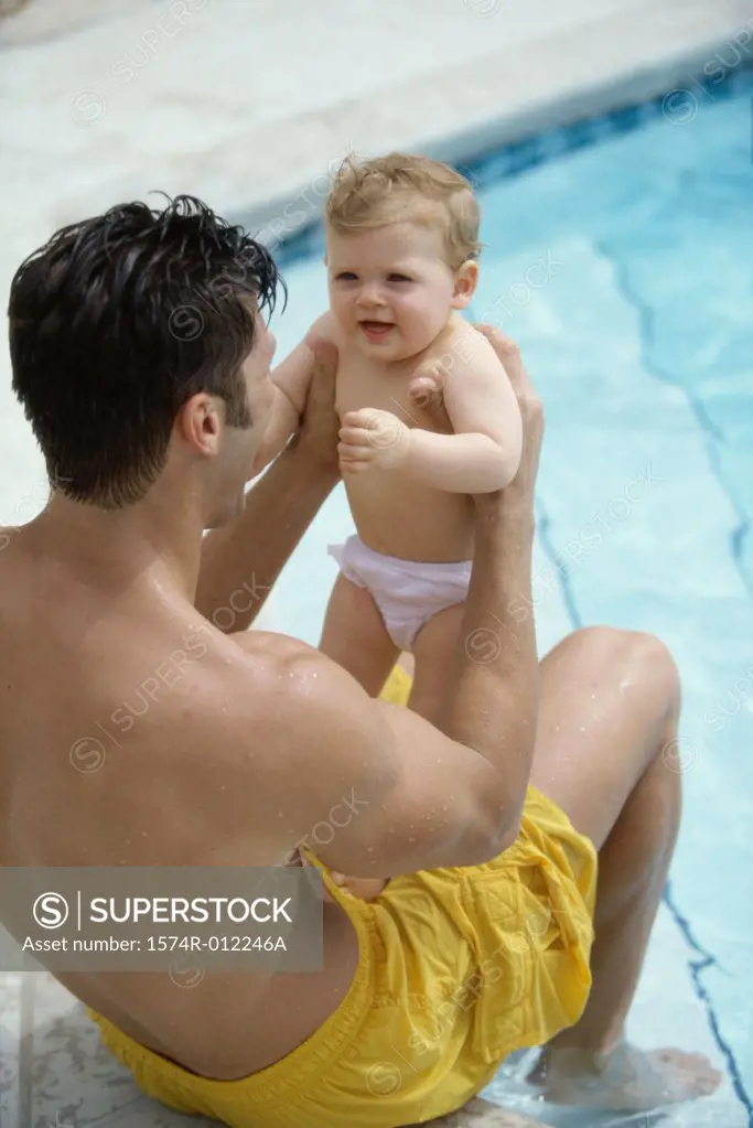 High angle view of a father sitting at the poolside playing with his son