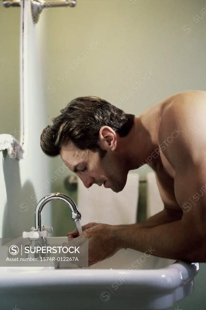 Side profile of a young man washing his face in a bathroom sink