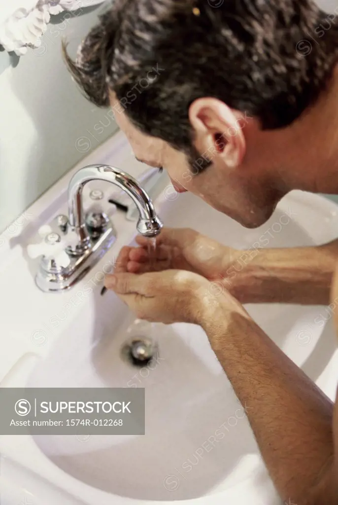 High angle view of a young man washing his face in the bathroom sink