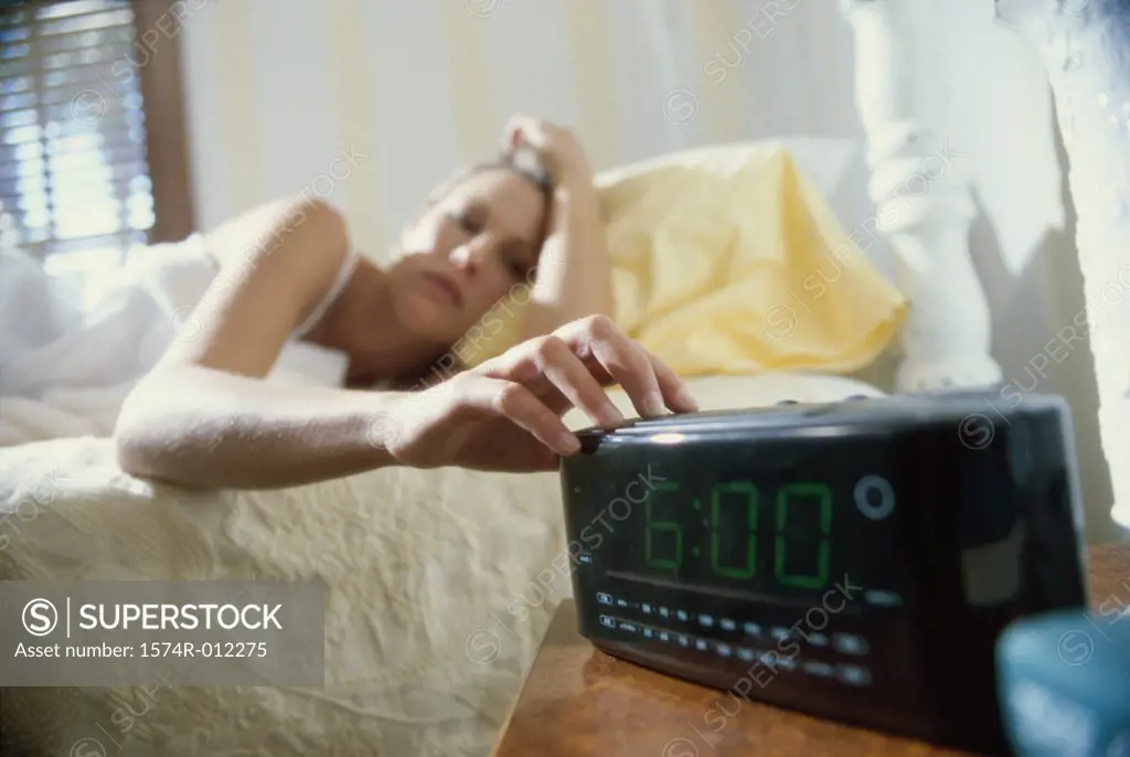 Young woman lying in bed reaching for an alarm clock