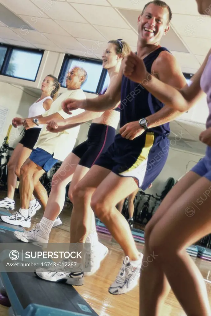 Side profile of five people doing step aerobics in a gym