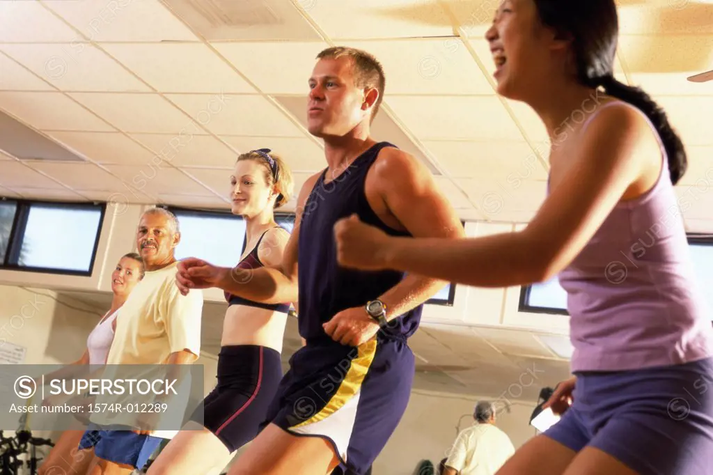 Side profile of five people doing step aerobics in a gym