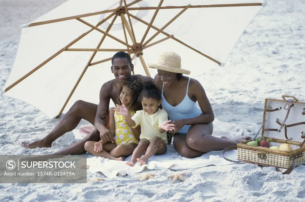 Parents and their two daughters sitting under a beach umbrella on the beach