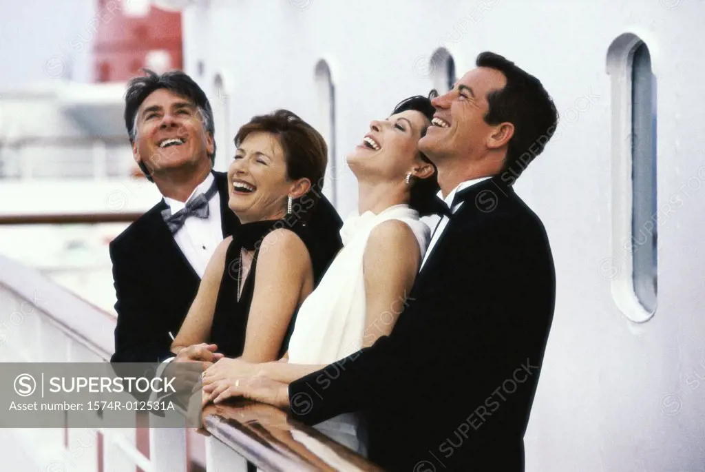 Mature couple and a mid adult couple standing on the deck of a cruise ship laughing