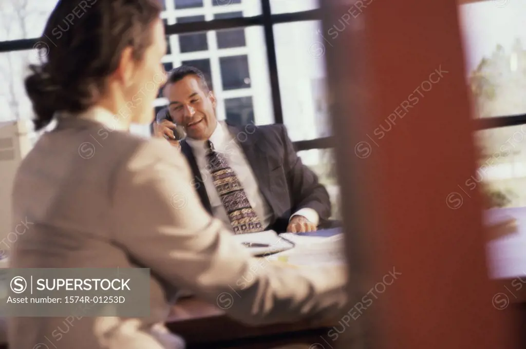 Businessman talking on a telephone sitting in front of a businesswoman