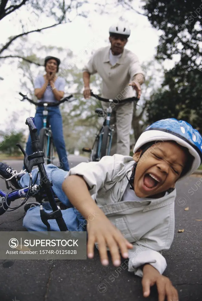 Close-up of a boy fallen off of a bicycle with his grandparents standing behind him