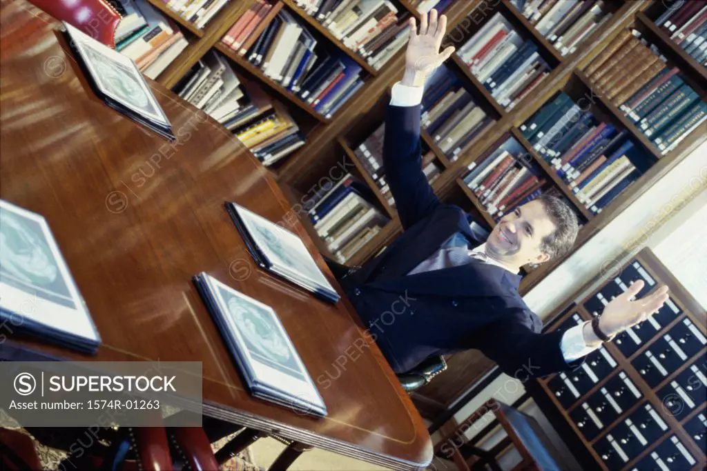 Businessman sitting in a library with arms raised