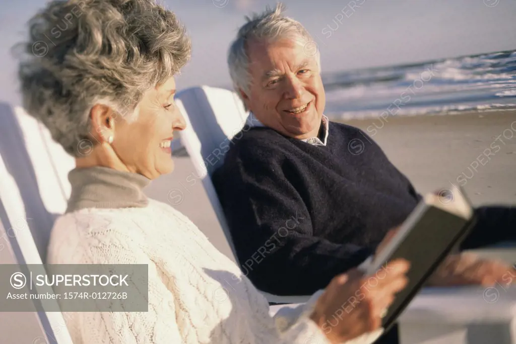 Senior woman reading a book with a senior man on the beach