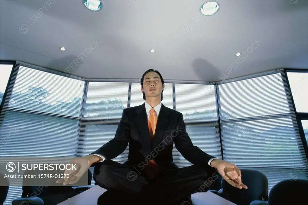 Businessman sitting in the lotus position on an office table