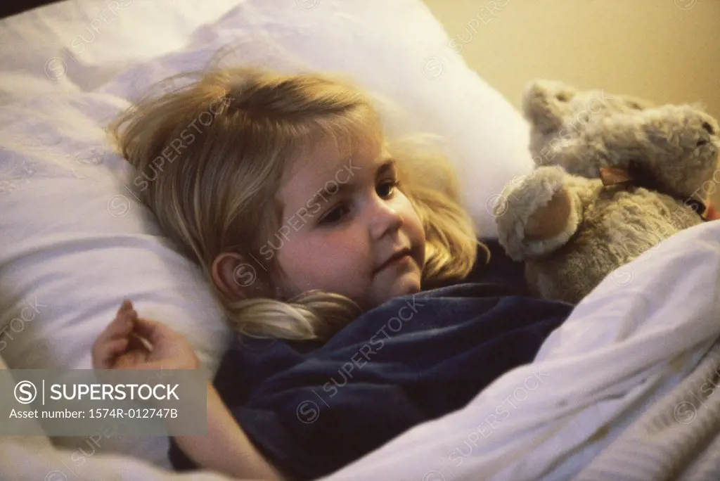 Close-up of a girl lying on the bed with her teddy bear