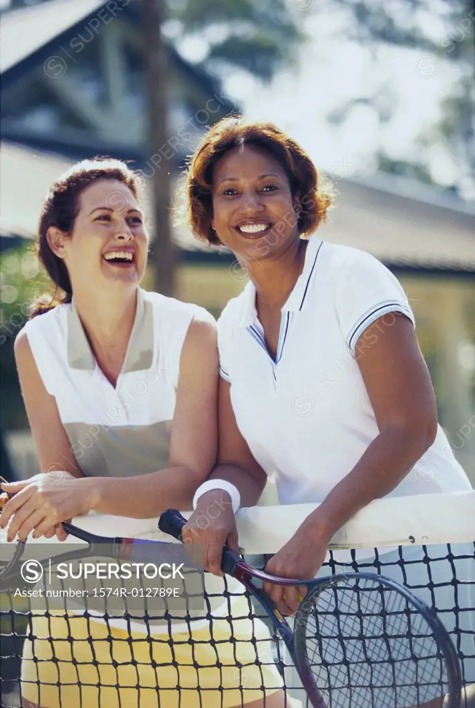Two mid adult women leaning against a tennis net