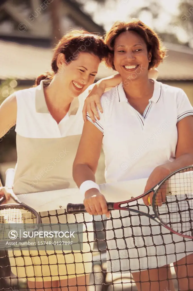 Two mid adult women leaning against a tennis net