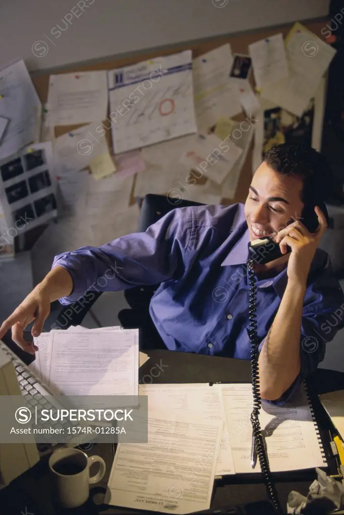 High angle view of a businessman talking on the landline telephone at his desk