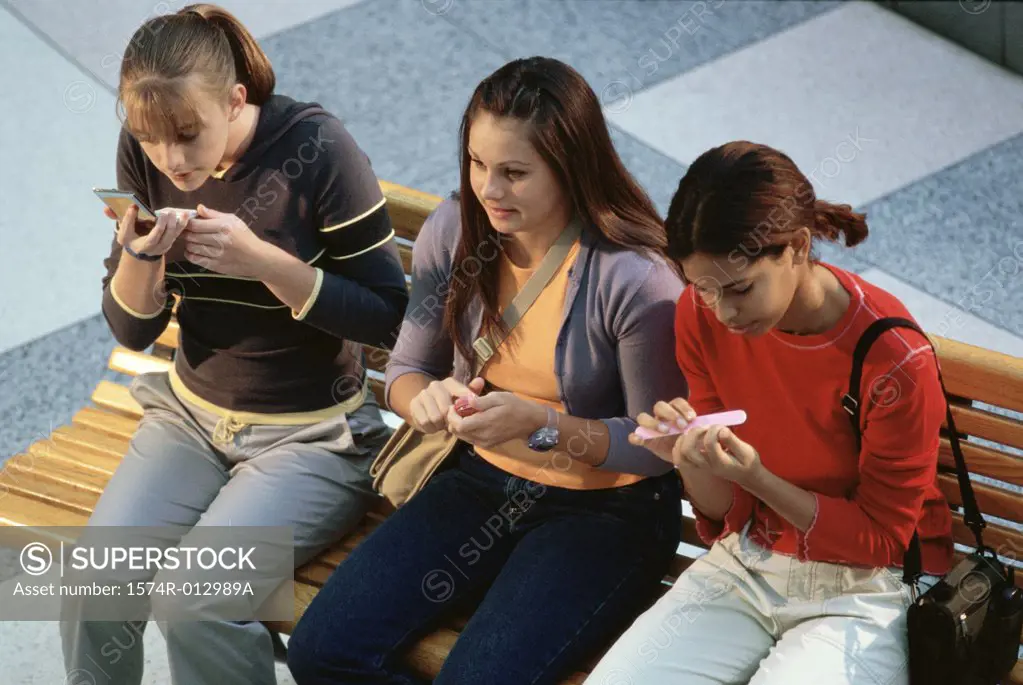 High angle view of three teenage girls sitting on a bench applying make-up