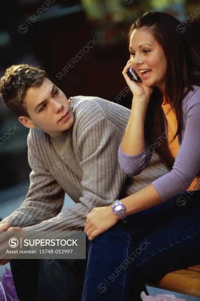 Teenage girl talking on a mobile phone with a teenage boy sitting beside her