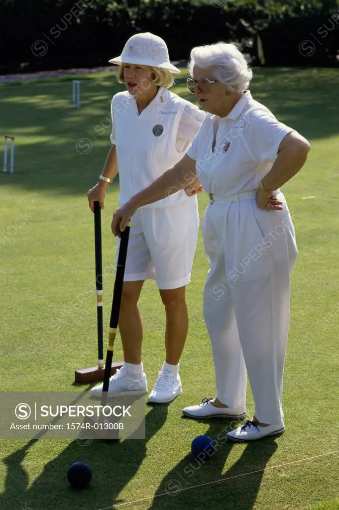 Two senior women standing on a lawn holding croquet mallets