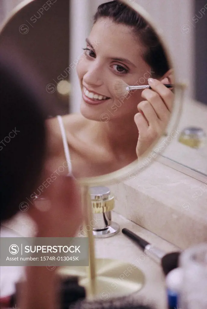 Reflection of a young woman applying blush with a make-up brush