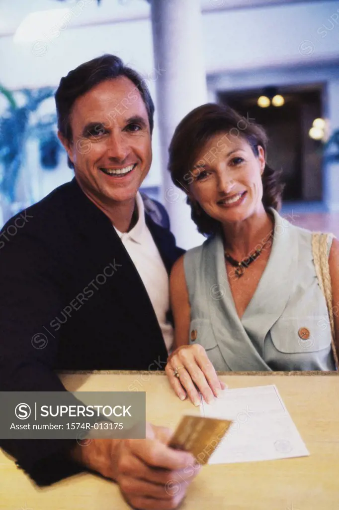 Portrait of a mid adult couple holding a credit card at a hotel reception desk