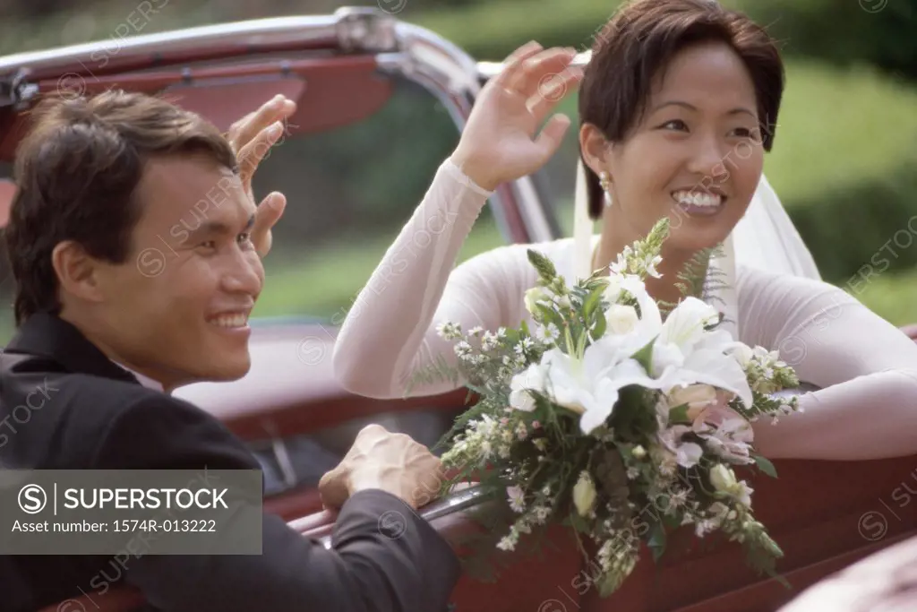 Close-up of a newlywed couple waving from a convertible car