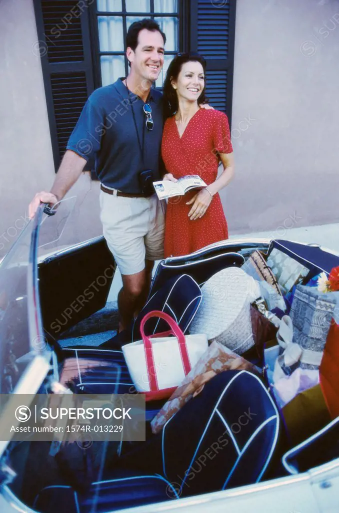 Mid adult couple standing near a convertible car and smiling