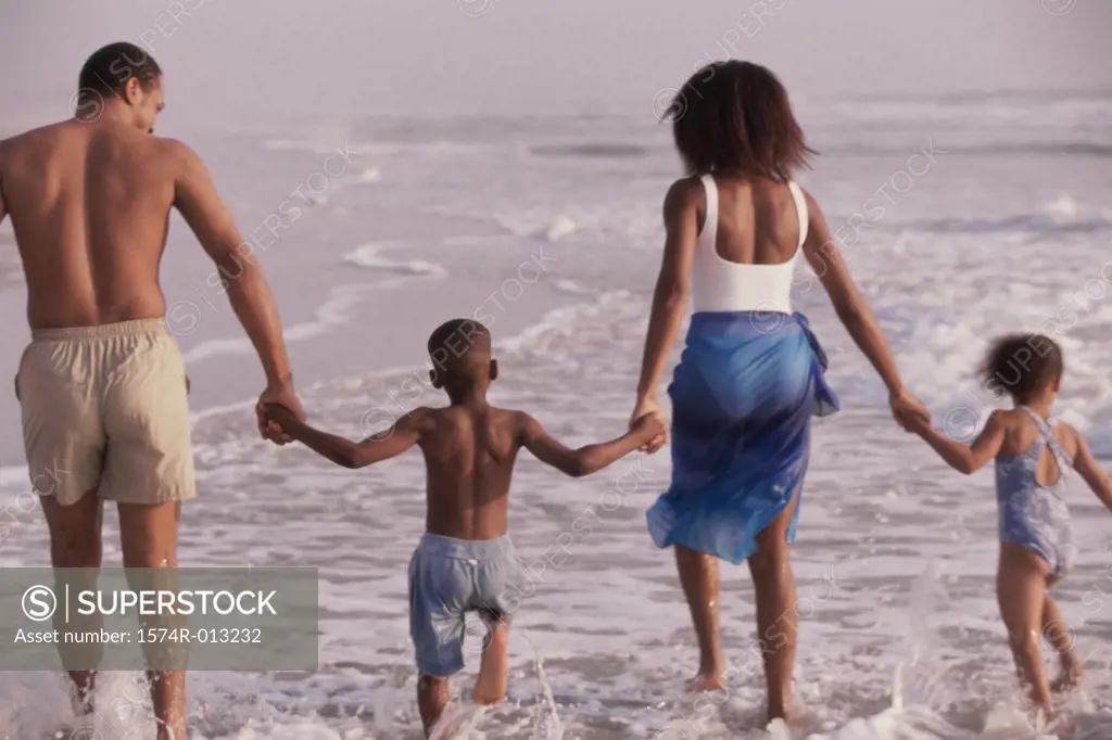 Rear view of parents and their two children walking on the beach