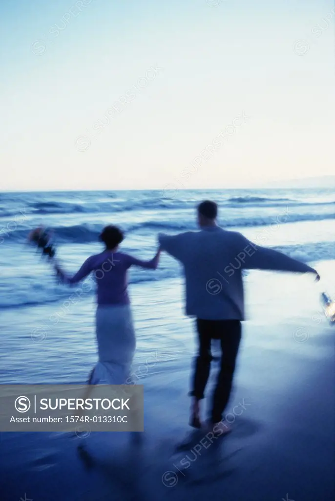 Rear view of a mid adult couple running on the beach