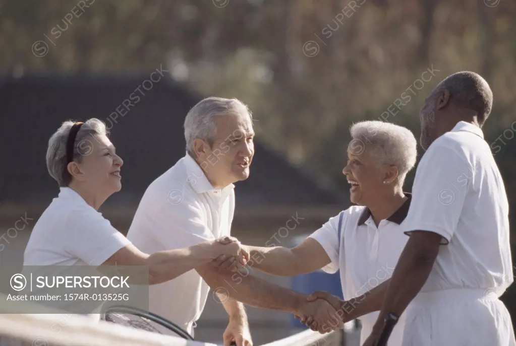 Side profile of two senior couples shaking hands on a tennis court