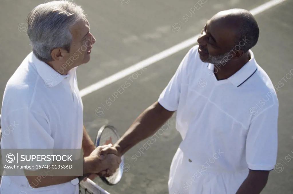 High angle view of two senior men shaking hands on a tennis court