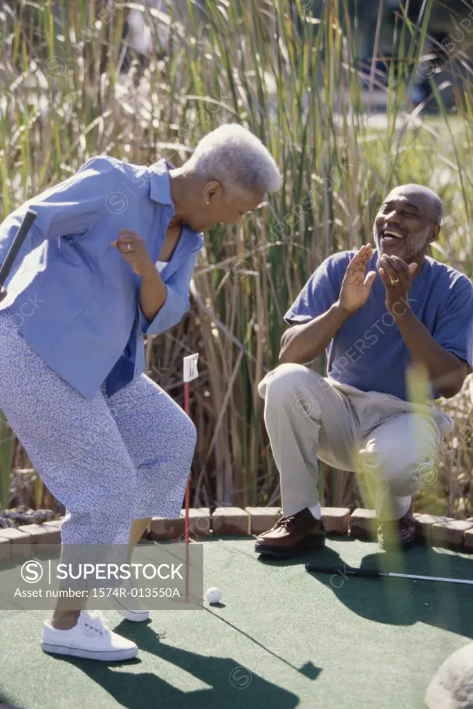 Senior man cheering a senior woman on a miniature golf course
