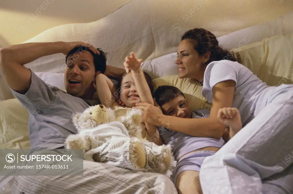 High angle view of parents and their two children playing in bed