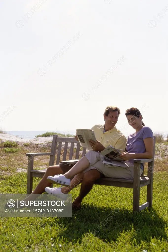 Mid adult couple sitting on a bench holding newspapers